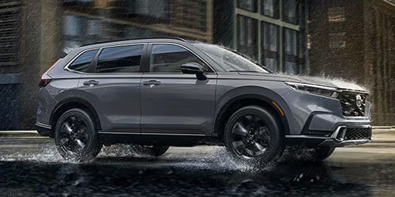 Gray Honda SUV driving through water on a city street with buildings in the background.