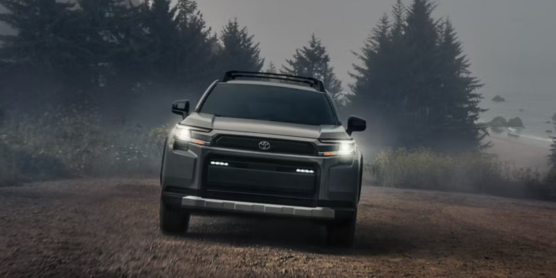 Front view of a gray Toyota SUV driving on a dirt road with fog and trees in the background.