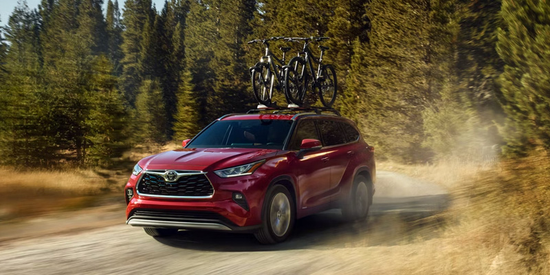 Red Toyota Highlander SUV driving on a forest trail with bicycles on the roof.