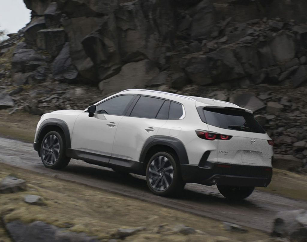 White Mazda CX-50 SUV driving along a rocky mountain road.